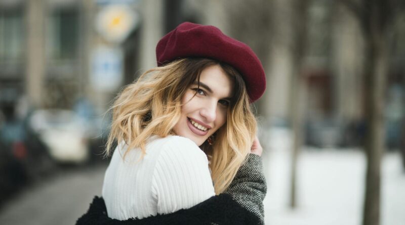 A joyful woman in winter attire with a burgundy beret, posing outdoors on a snowy day.